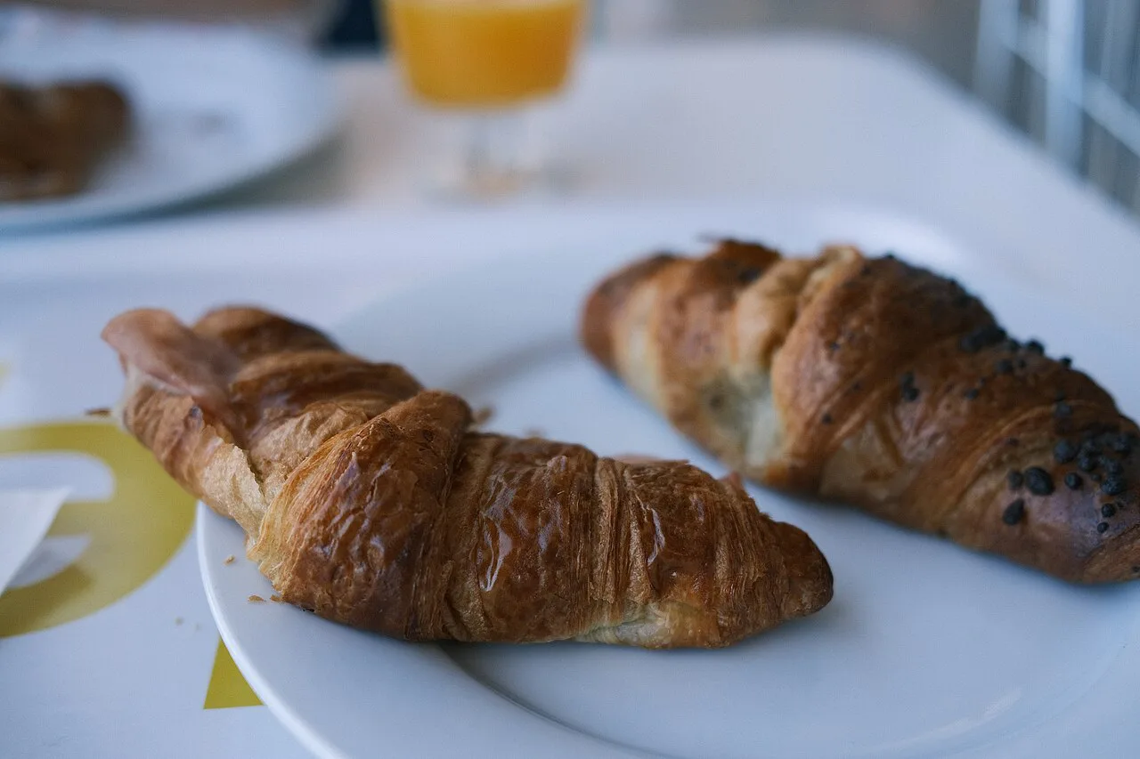 Two croissants on a plate with a glass of juice.