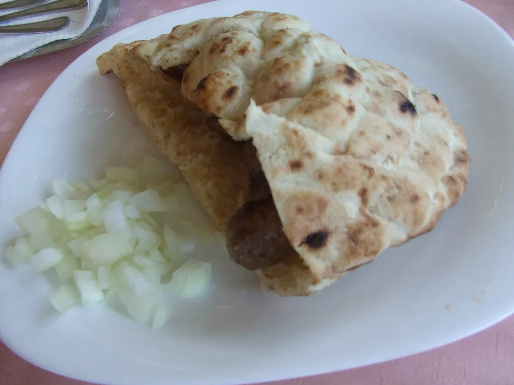 Ćevapi in somun flatbread with chopped onion.