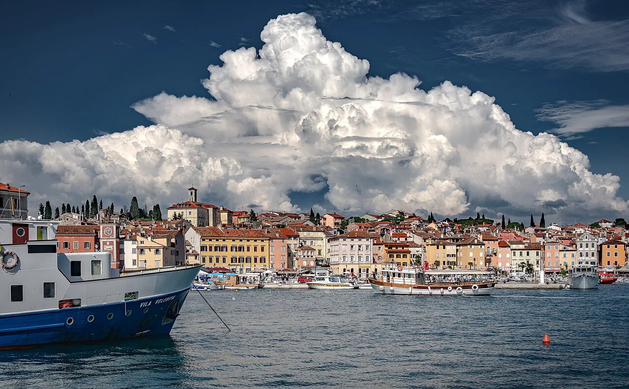 Rovinj harbour under a towering cloud.