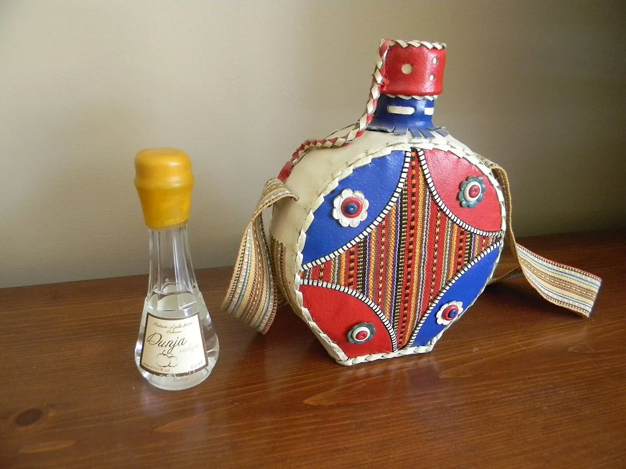 A decorated rakija flask beside a small rakija glass.