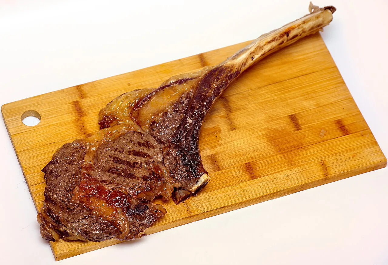 A grilled tomahawk steak on a wooden board.